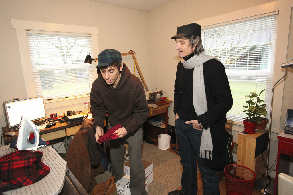 Santi showing a friend a length of red plaid fabric in the living room